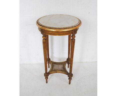 A marble topped gilt occasional table, raised on fluted legs with cane work shelf under - diameter 45cm, height 74cm