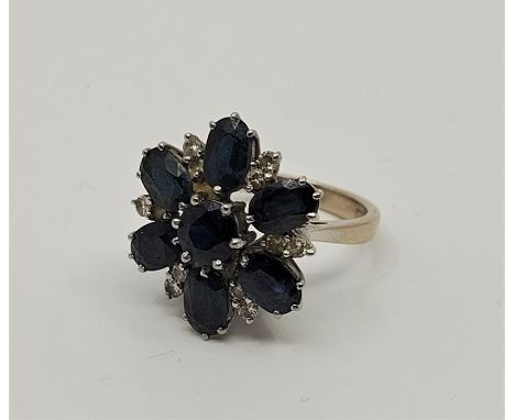 An 18ct. white gold, sapphire and diamond cluster ring,&nbsp;the flower form mount set mixed round cut sapphire to raised cen