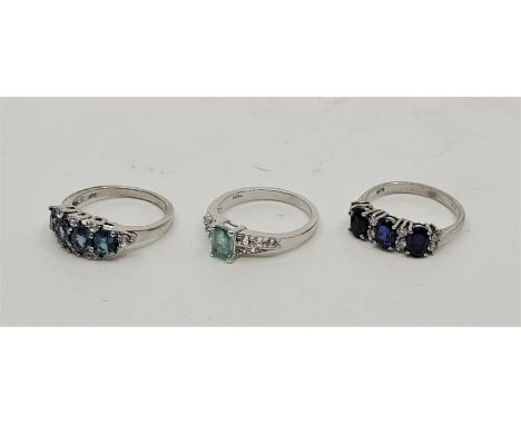 Three silver rings set various gemstones, to include: a silver, emerald and white topaz set ring, a silver and blue topaz set