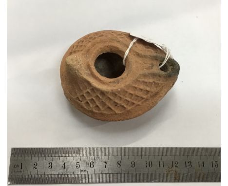                        Roman pottery oil lamp of a red colour. It is 87 mm long by 71 mm wide. It is of the later more bulbo