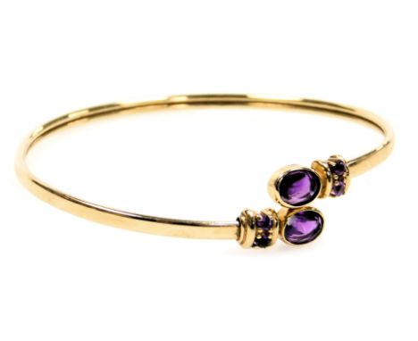 A 9ct gold and amethyst set torc bangle, set with a pair of oval cut amethysts, and four brilliant cut amethysts, 8.1g.