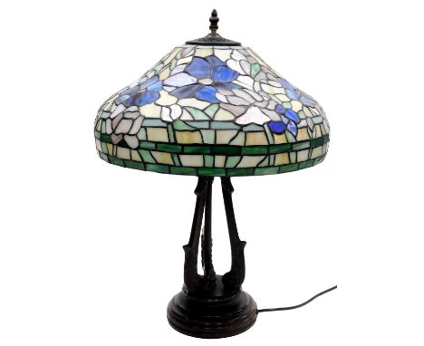 A Tiffany style table lamp, shade decorated with flowers, raised on a bronzed plaster base, with leaf cap scroll supports, 58