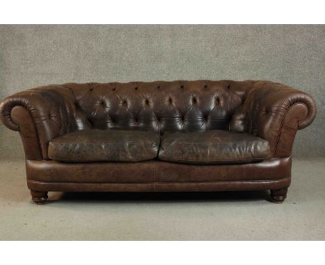 A contemporary brown leather Chesterfield sofa, with buttoned scrolling arms and back, on turned feet. H.70 W.185 D.90cm. 