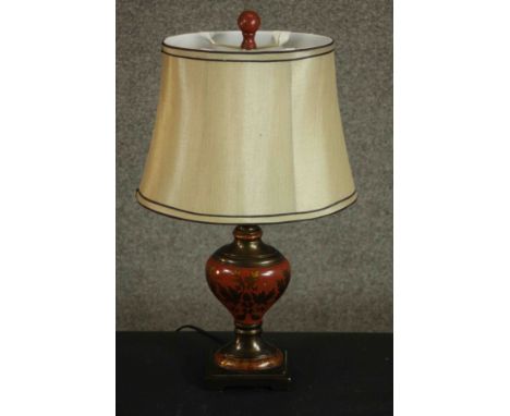 A toleware table lamp, of baluster form and painted with gilt foliate designs on a red ground, with a shade. H.52 W.32 D.22cm