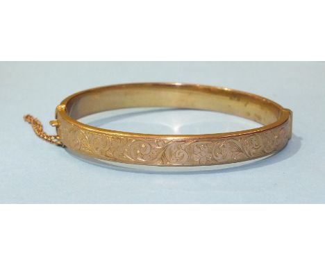 A 9ct yellow gold hinged bangle with engraved scroll decoration, 9.4g, (dent to front).