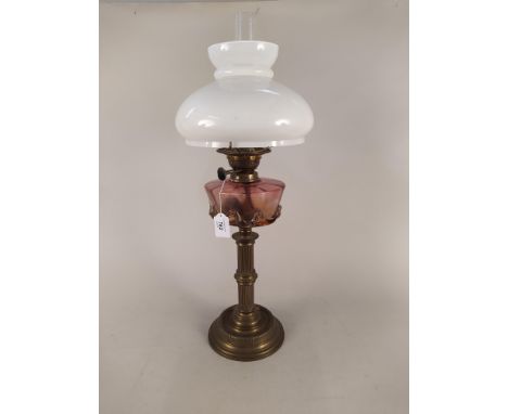 An antique brass oil lamp with cranberry glass reserve and white glass shade