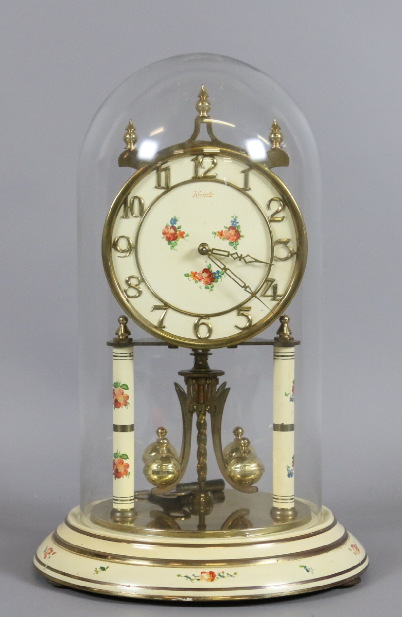 A Kundo anniversary clock under glass dome decorated with flowers.