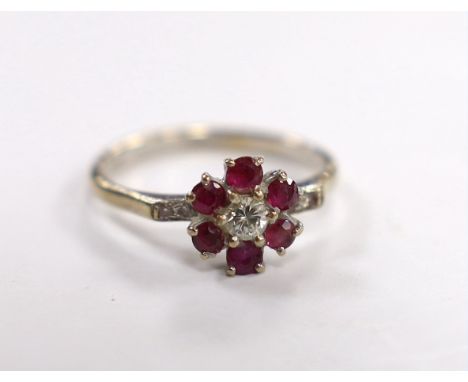 An 18ct white metal, ruby and diamond cluster set flower head ring, with diamond chip set shoulders, size I, gross weight 3.1