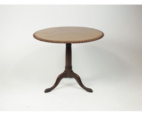 A George III mahogany tripod table the circular top with gadrooned border, raised on a gun barrel column and three down carve