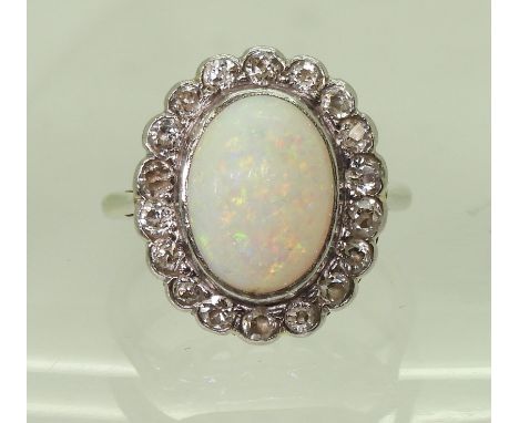 A white opal & diamond cluster ring, mounted in white metal, set with a central oval cabochon opal, surrounded with a ring of