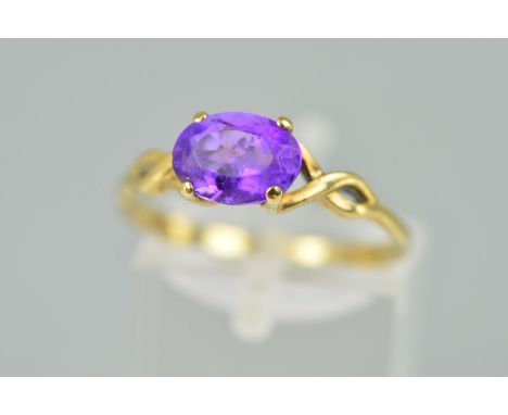 A 9CT GOLD AMETHYST RING, designed as an oval amethyst within a four claw setting to the open crossover design shoulders, wit