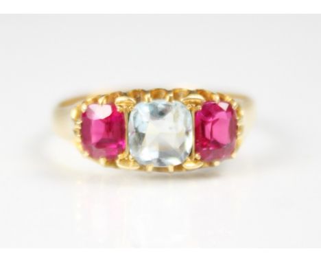 An aquamarine and synthetic ruby three stone ring, the central cushion cut aquamarine with a cushion cut synthetic rubies to 