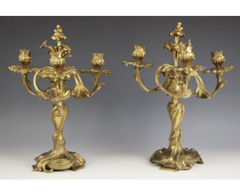 A pair of polished cast brass Rococo revival three branch candelabra, 19th century, the candle sconces set to scrolling acant
