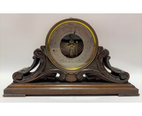 A brass cased aneroid barometer, upon carved and pierced oak leaf scroll stand, the 4.25 inch silvered engraved dial signed '