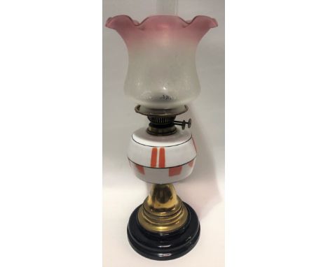 A brass oil lamp with white opaque glass reservoir and cranberry blush etched shade and on black pottery socle, height to sha