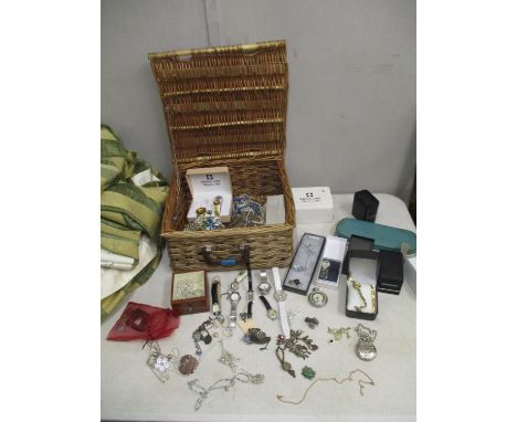 A wicker basket containing a selection of costume jewellery and wristwatches, to include a silver charm bracelet, and a 9ct g