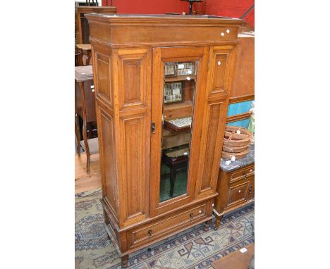 An early 20th century oak bedroom suite, comprising wardrobe, stepped cornice, central mirrored door flanked by fielded panel