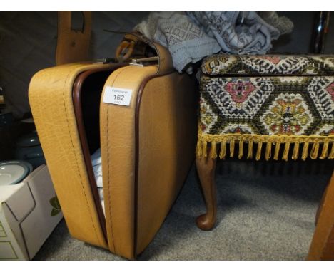 A VINTAGE SUITCASE CONTAINING LINEN TOGETHER WITH AN UPHOLSTERED FOOTSTOOL/ SEWING BOX 
