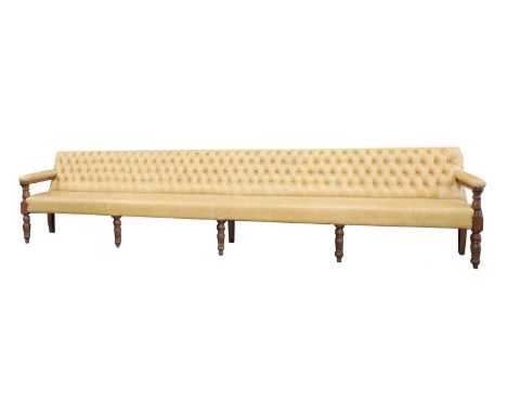 A long leather upholstered bench,late 19th century/early 20th century, the button back and open arms and over-stuffed seat, u