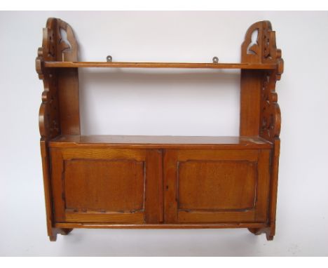 A late Victorian ash wall hanging cabinet, with open shelf over a pair of cupboard doors and foliate pierced sides.
61cm high