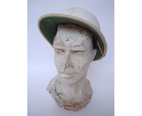 A plaster bust of man, 27cm high together with a French pith helmet, bearing label 'Au petit Paris, 22 Avenue William Ponty, 