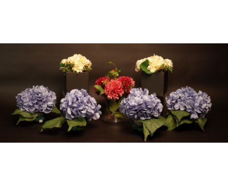 A faux flower arrangement of ivory roses and sweet peas in a cylindrical glass pot, faux hydrangeas in square ceramic pots, f