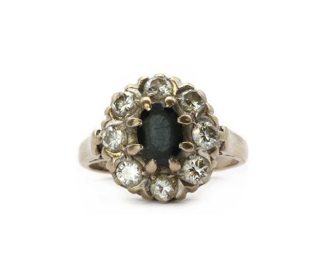 A white gold sapphire and diamond cluster ring,an oval mixed cut sapphire, claw set, to a surround of brilliant cut diamonds,