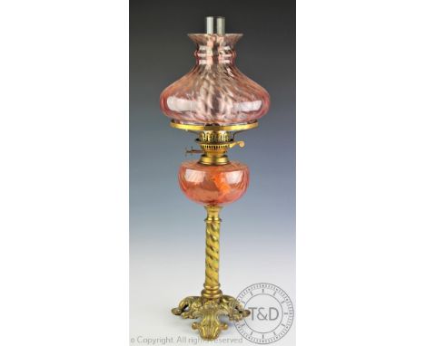 A Victorian oil lamp with cranberry glass shade, raised on a twisted brass column upon a cast trefoil base, with burner and f