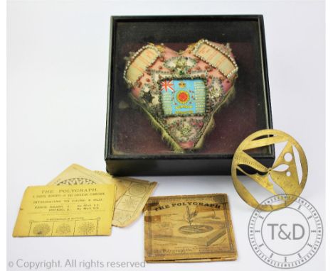 A World War One heart shaped pin cushion, set with glass beads, badges etc,in an ebonised case, case 25cm wide; with a vintag