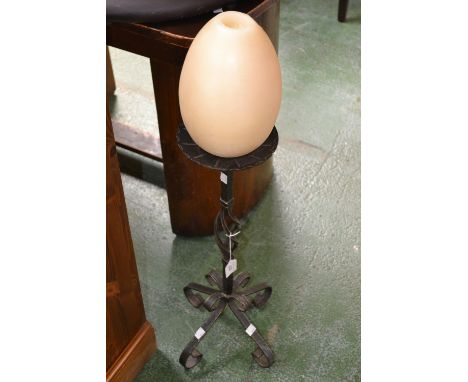 A wrought iron floor standing candlestick with large egg shaped candle 