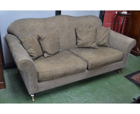 A Wesley Barrell Hinton three seat sofa of large proportions, shaped back, scrolling arms, turned forelegs, brass casters.