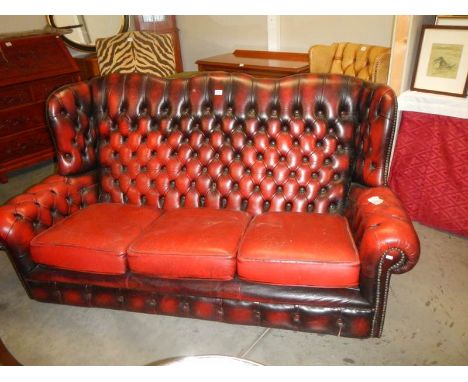 A 20th century deep buttoned blood red leather three seat winged sofa, COLLECT ONLY.