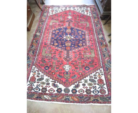 A red ground Oriental Rug with blue central lozenge with double arrow heads surrounded by deer and stylised figures within gr