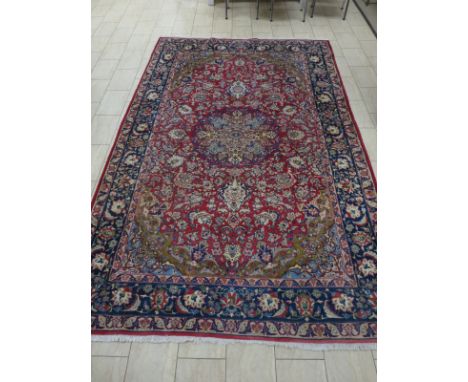 A red ground Carpet with central floral motif surrounded by trailing floral decoration with blue tramline borders, 12ft 9in x