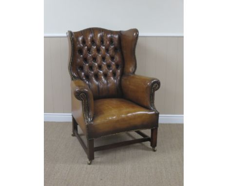 A Georgian style brown leather button back Wing Armchair on square supports and brass casters