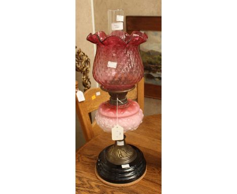 A late Victorian oil lamp with double wick, fitted with Cranberry glass shade, opaline glass reservoir, brass cast spreading 