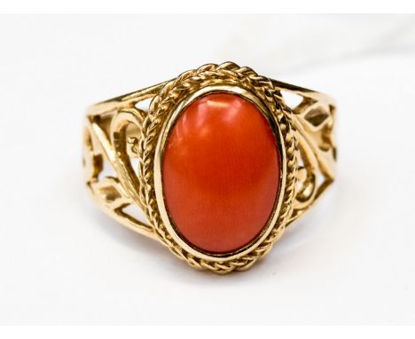 A 9ct. gold ring set coral in pierced scroll shoulders