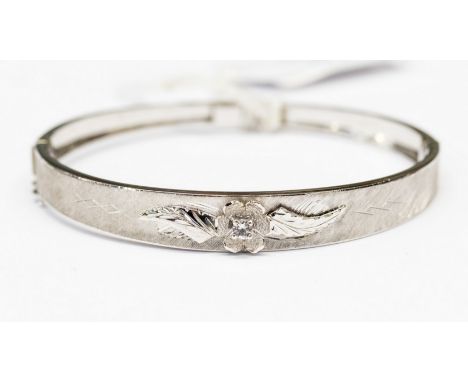 An eighteen carat white gold, round hinged bangle stamped 750 and set with a single white stone, in an applied flower and lea