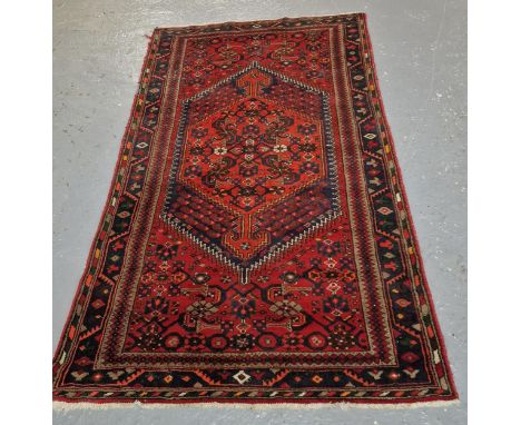 Vintage Shiraz red and navy ground rug, with central geometric medallion and stylised foliate and geometric repeating designs