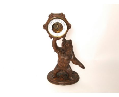 A late 19th century carved Tyrolean bear holding aloft a hexagonal frame incorporating an eneroid barometer, with German scri