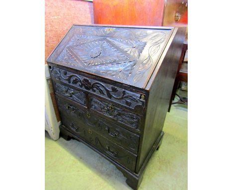 A small Victorianised oak bureau, the front elevation with carved foliate and further detail, the fall flap enclosing a fitte