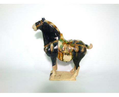 An oriental reproduction ceramic model of a Tang style horse with predominantly dark blue glaze with green and ochre coloured