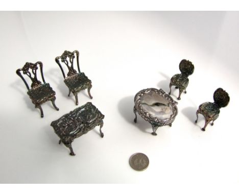 A collection of miniature silver salon furniture, 4 chairs, sofa and two tables, all with embossed cherub and other detail, 5