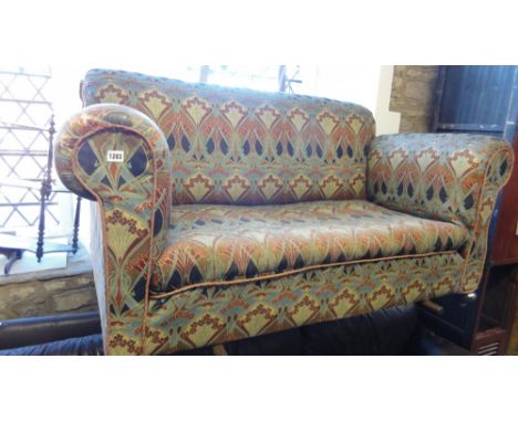 An Edwardian two seat sofa with rolled arms, single drop end, upholstered in Liberty stylised floral patterned fabric and rai