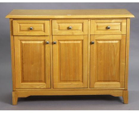 A light oak/ash sideboard fitted three frieze drawers above cupboards enclosed by three fielded panel doors, &amp; on short s