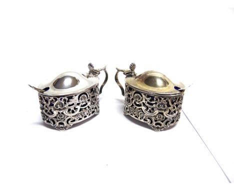 A PAIR OF LATE VICTORIAN SILVER PIERCED AND EMBOSSED OVAL MUSTARD POTS each with a double scroll handle, a domed and hinged l
