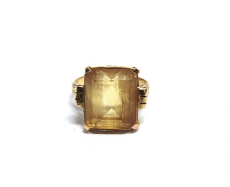 A CITRINE SINGLE STONE RING  the rectangular step-cut stone claw set in yellow metal between emerald shoulders on a plain sha