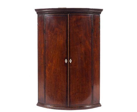 A George III mahogany and inlaid bow-fronted hanging corner cupboard:, with a moulded cornice and interior fixed shelves encl