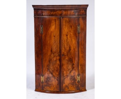 A George III mahogany bow-fronted hanging corner cupboard:, with a moulded cornice, the interior with three fixed shelves and