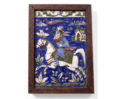 A PERSIAN POTTERY TILE decorated a huntsman on horseback on a dark blue ground, framed, 23.5 x 16cm